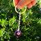Deep purple Amethyst keychain with silver wire wrap, shown in hand outdoors in front of green bush for natural contrast.